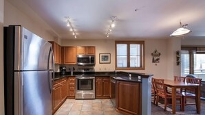 A modern kitchen with stainless steel appliances, wooden cabinets, and a dining area with a table and chairs. - Premium Unit 1327 - One Bedroom - Zephyr Mountain Lodge 1 Condo (Winter Park)