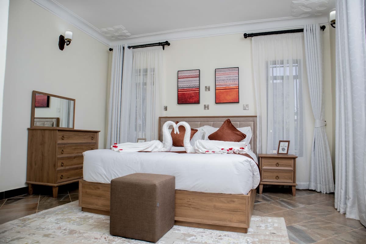 Un dormitorio ordenado con una cama grande, un aparador de madera, una mesita de noche y un espejo.