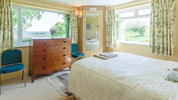 A bedroom with a bed, dresser, two chairs, and a window with curtains. - Curlew Cottage (Hexham)