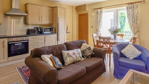 A compact living space with a kitchenette, a brown sofa, a blue armchair, and a dining area with a table and chairs. - Curlew Cottage (Hexham)