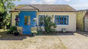 A quaint cottage with a blue door and windows, surrounded by potted plants and a gravel driveway. - Curlew Cottage (Hexham)