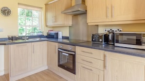 A kitchen with wooden cabinets, a stainless steel range hood, a microwave, a toaster, and a clock on the wall. - Curlew Cottage (Hexham)