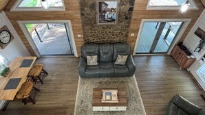 A spacious loft with a stone wall, a leather sofa, wooden flooring, and large windows.