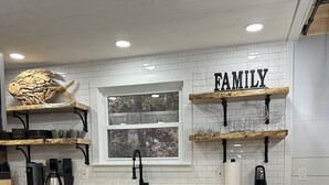 A modern kitchen with blue cabinets, a stainless steel dishwasher, and wooden shelves displaying glasses and a fish decoration.