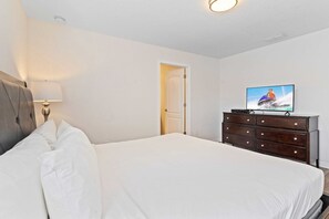 A hotel room with a bed, a dresser, a television, and a door. - Disney Getaway: 3BR Kissimmee Resort Pool Townhome (Kissimmee)
