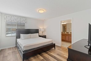 Et soveværelse med seng, sengebord, lampe og udsigt til køkkenet.