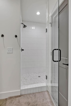 Una ducha moderna con puerta de vidrio, paredes cubiertas de azulejos blancos y un escalón que da acceso al área de la ducha.