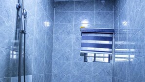Une petite salle de bain moderne, équipée d’une douche, de toilettes et d’une fenêtre avec stores.