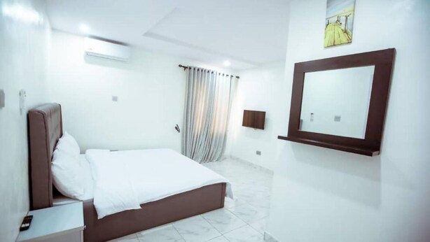 A hotel room with a bed, a bedside table, a mirror, and a window with curtains.