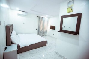 A hotel room with a bed, a bedside table, a mirror, and a window with curtains.