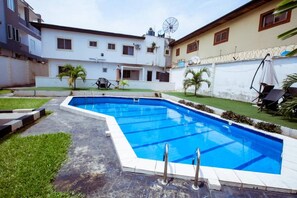 A rectangular swimming pool with a tiled edge, surrounded by a paved area and grass. - Stunning 2-bed Apartment in Lagos (Lagos)