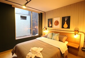A bedroom with a large bed, a window, and wall art. - One Living by Roots Rentals (Medellín)