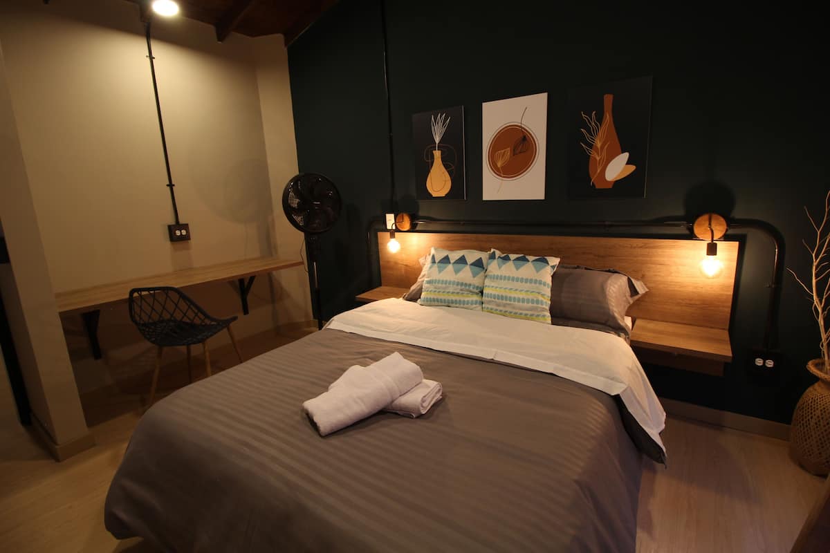 Un lit bien fait, avec une serviette pliée, une tête de lit en bois et des lampes fixées au mur.