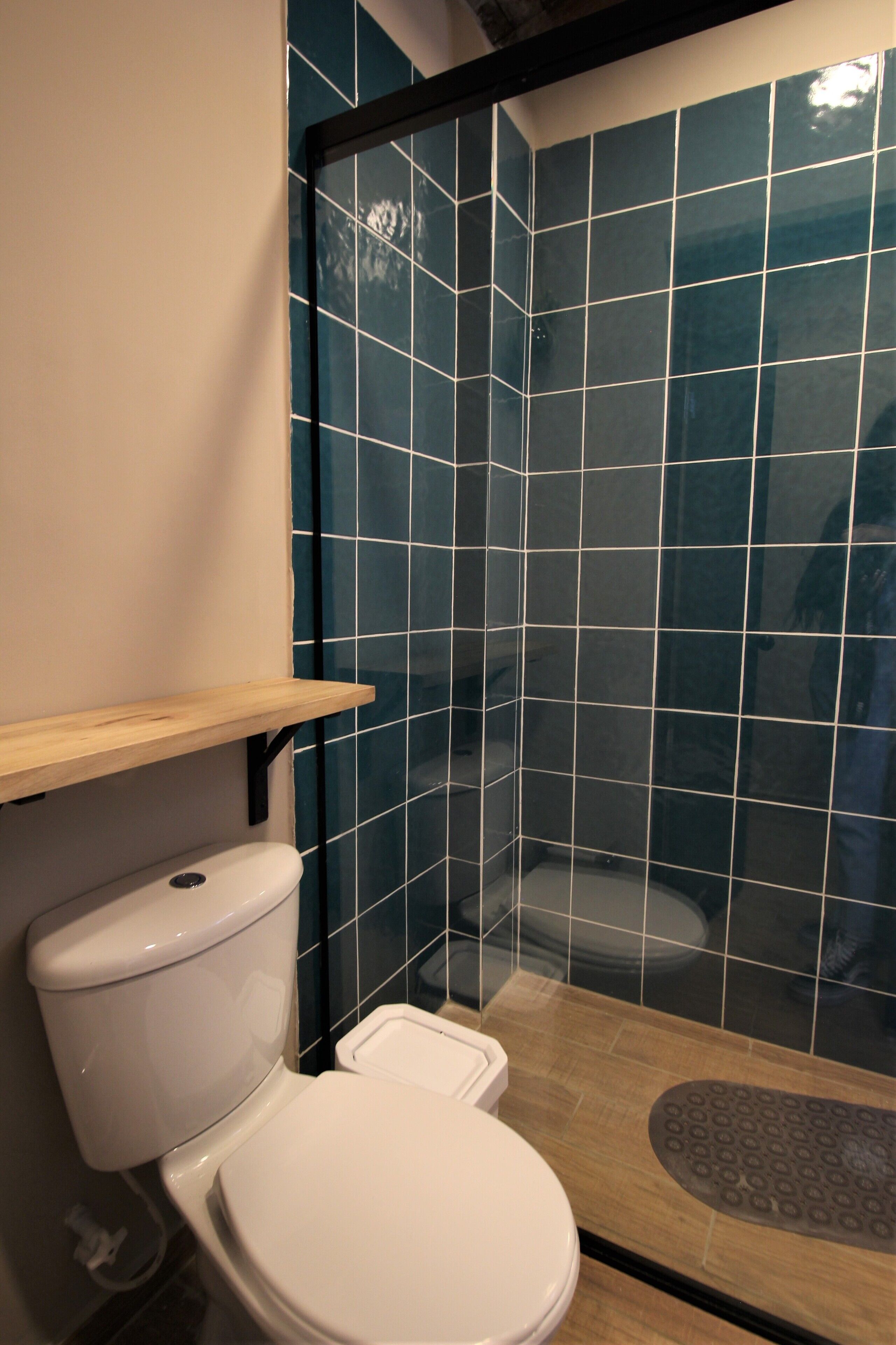 Ein Badezimmer mit Toilette, einem Holzregal und einem Duschbereich mit dunkelblauen Fliesen.