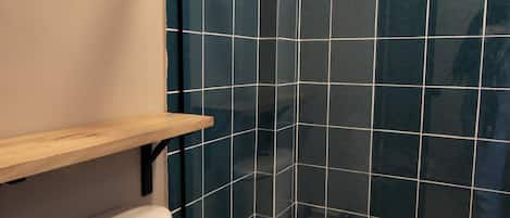 Ein Badezimmer mit Toilette, einem Holzregal und einem Duschbereich mit dunkelblauen Fliesen.