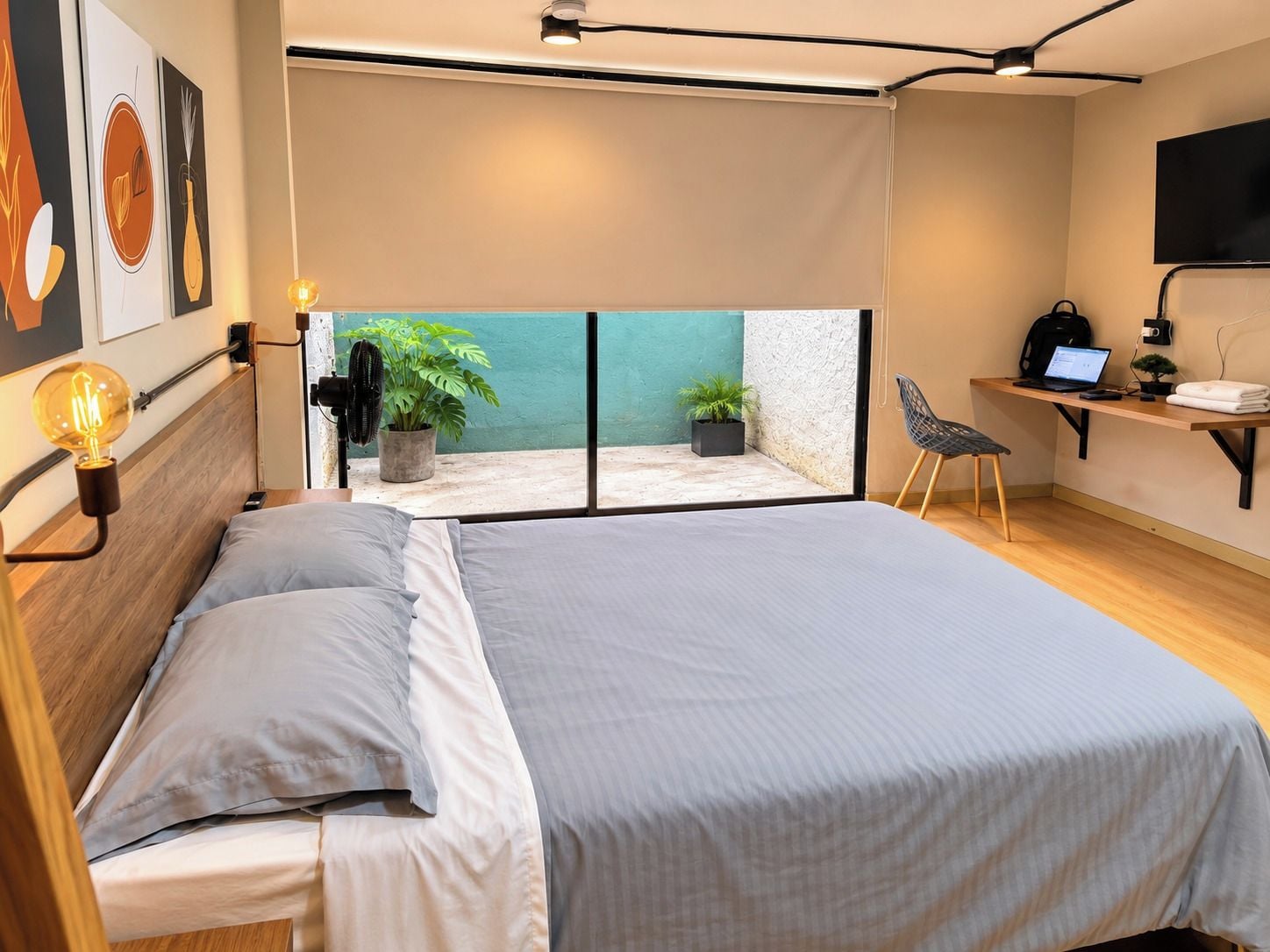 Un dormitorio moderno con una cama grande, un escritorio con una laptop, una silla y un balcón con plantas.