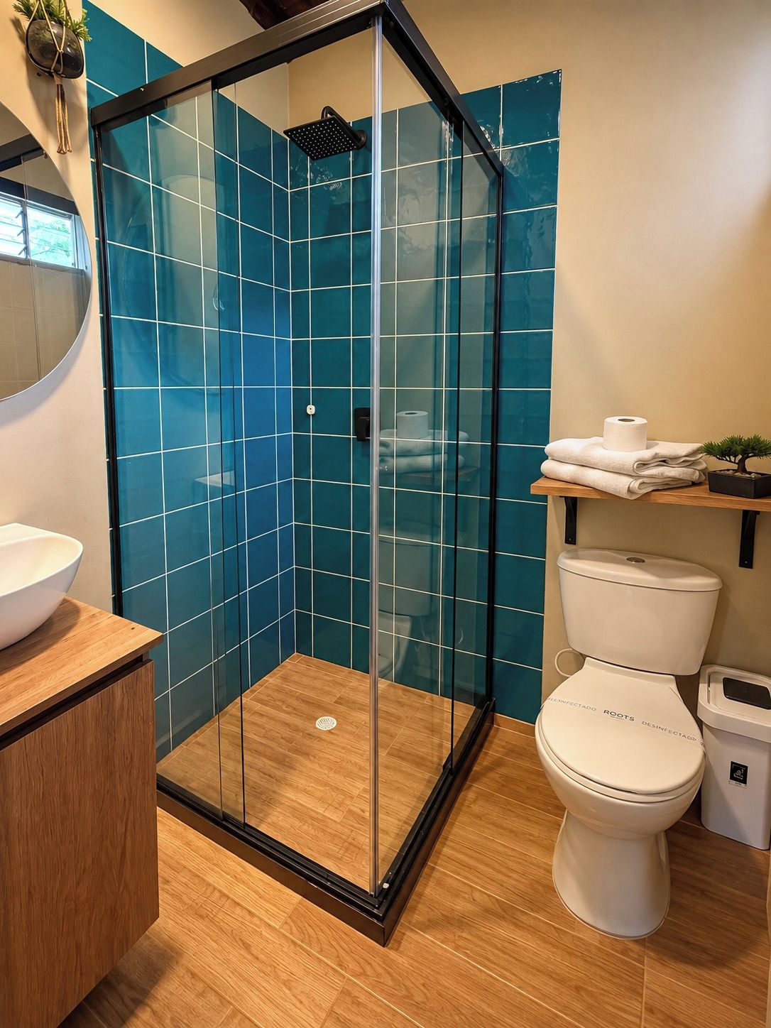 Een moderne badkamer met een glazen douchecabine, een wit toilet en een houten wastafelmeubel met een waskom.