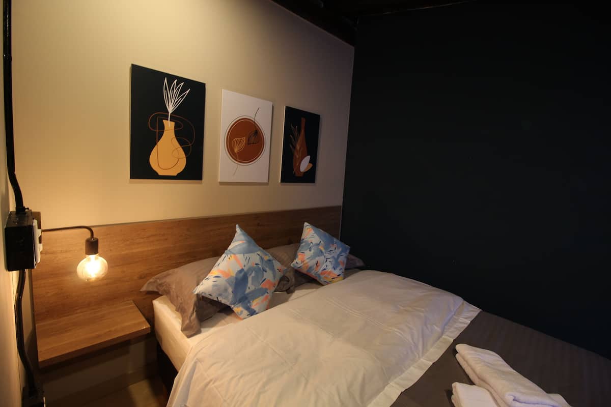 Une chambre d’hôtel avec une tête de lit en bois, un lit recouvert de draps blancs et agrémenté de deux coussins à motifs, et trois œuvres d’art encadrées accrochées au mur.