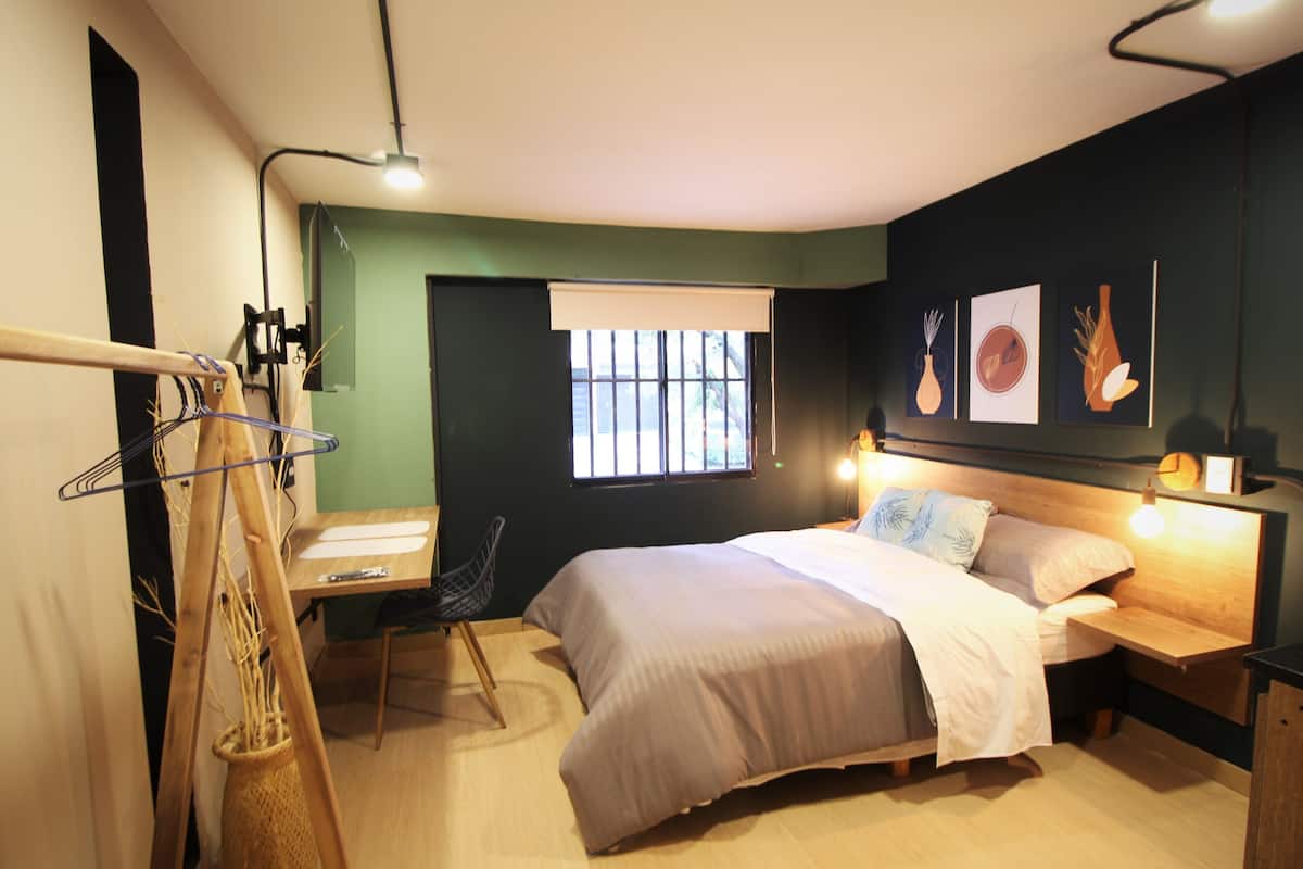 Une chambre à coucher comprenant un lit, une table de chevet, une lampe, une fenêtre et un bureau avec une chaise.