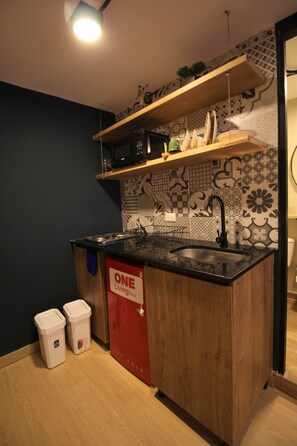 A compact kitchen with a black countertop, wooden cabinets, a stainless steel sink, and patterned backsplash tiles.