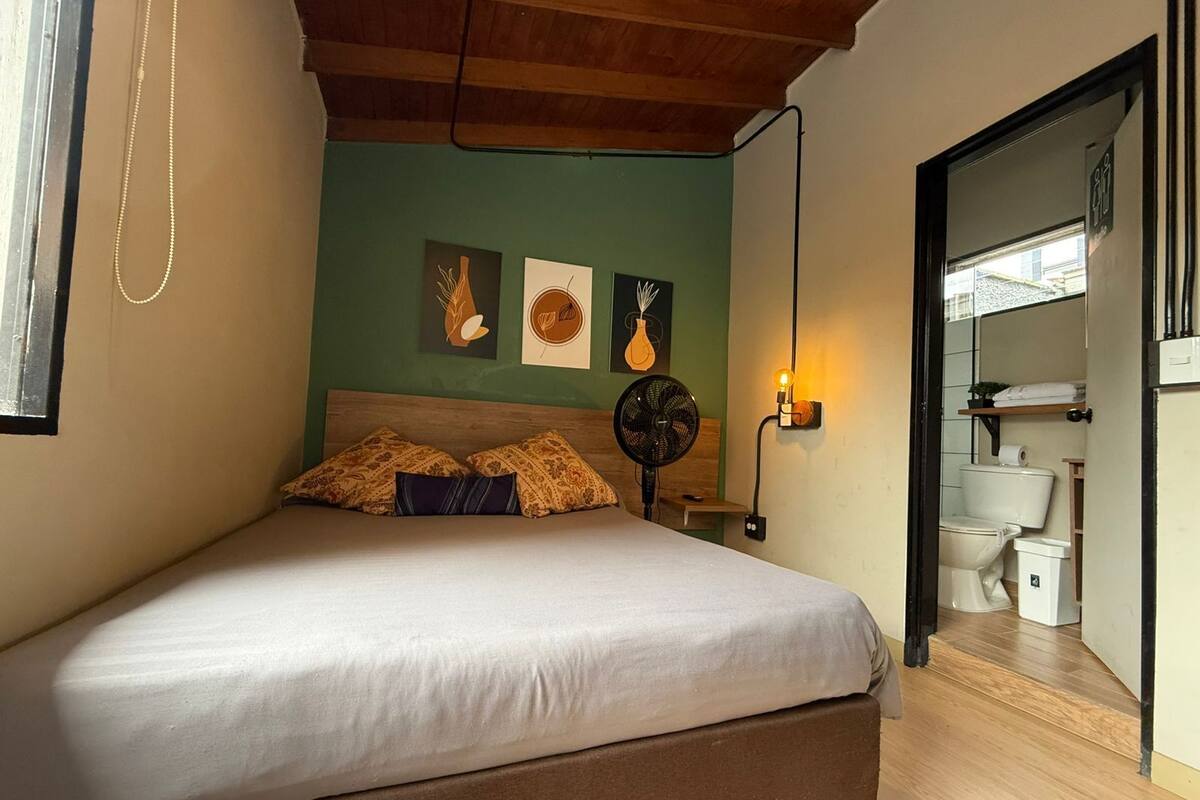 Une chambre à coucher avec un lit, un ventilateur fixé au mur et des œuvres d’art.
