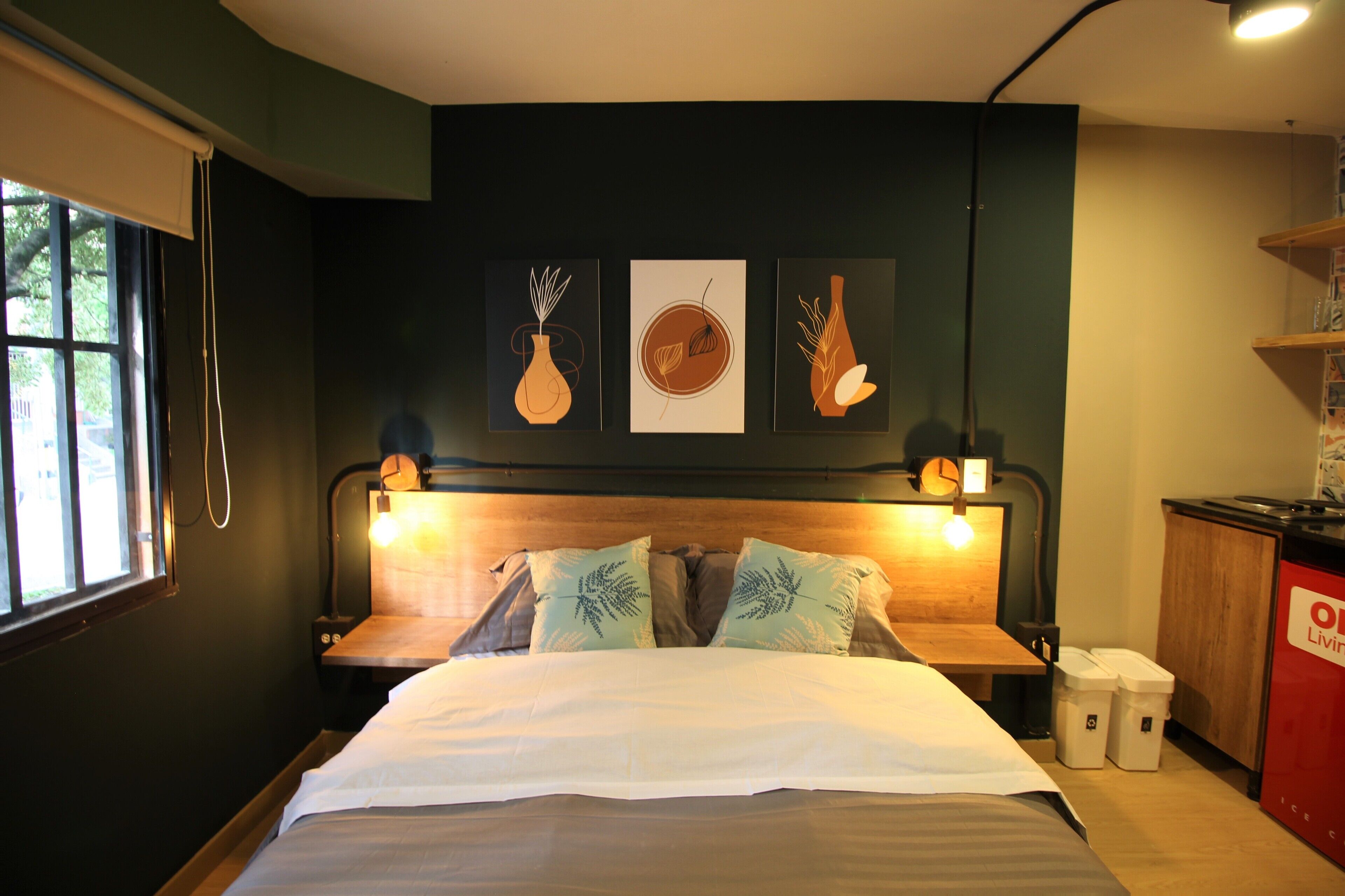 Un lit bien fait, avec une tête de lit, deux tables de chevet et une petite table d’appoint. Trois œuvres d’art encadrées sont accrochées au mur au-dessus du lit.