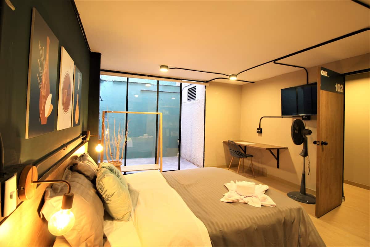 Une chambre d’hôtel moderne équipée d’un lit, d’un bureau, d’une chaise, d’une télévision et d’une porte-fenêtre coulissante donnant sur un balcon.