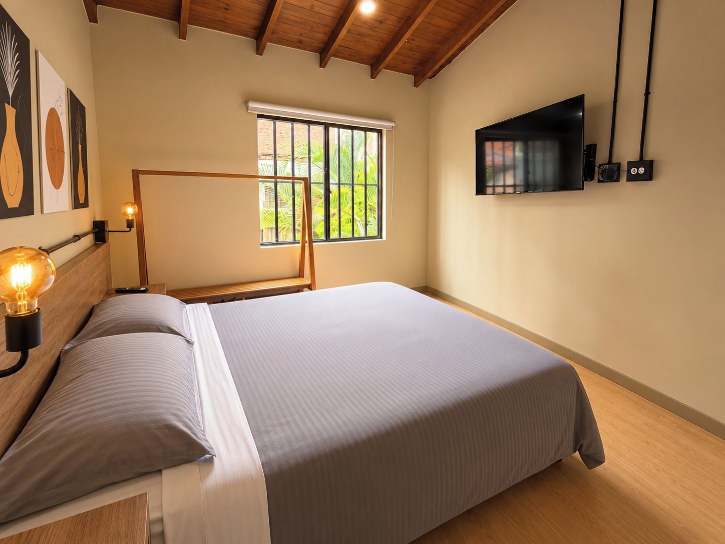Une chambre à coucher avec un lit, une lampe de chevet, un téléviseur et une fenêtre donnant sur un paysage verdoyant.