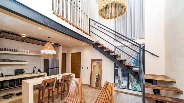 Une cuisine moderne dotée d’un îlot central, de chaises en bois et d’un escalier avec une rampe noire.