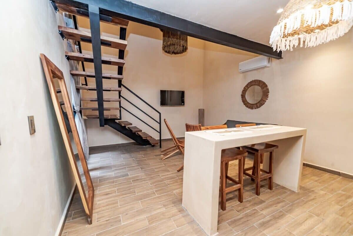 Ein modernes Interieur mit einer Treppe, einem Essbereich mit weißem Tisch und Holzstühlen sowie einer hängenden Leuchte.