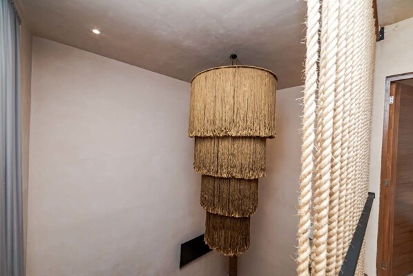 A multi-tiered rope chandelier in a hallway with plain walls and a wooden door.