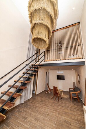 Un intérieur moderne avec un escalier en bois, un luminaire suspendu en fibres tressées et un espace en mezzanine aménagé avec des sièges.