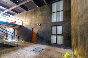 Un interno spazioso con soffitto alto, pareti in cemento e ampie finestre.