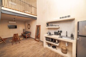 Une cuisine compacte dotée d’un évier encastré, de chaises en bois, d’un miroir et d’un luminaire suspendu.