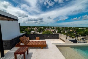 A rooftop terrace with a pool, wooden furniture, and a view of a town. - Downtown Tulum Loft w/Rooftop Pool (Tulum)