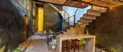 A modern interior with a concrete staircase, a table with stools, and a ceiling made of wooden slats.