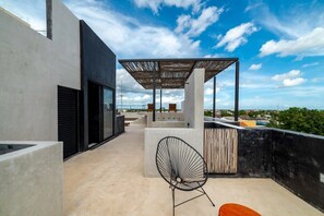 A rooftop terrace with a modern design, featuring a concrete structure, a wooden pergola, and a black wire chair. - Downtown Tulum Loft w/Rooftop Pool (Tulum)