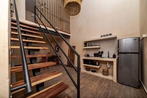 A modern kitchen with a built-in refrigerator, wooden staircase, and a hanging light fixture.