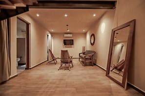 Une pièce spacieuse avec un plancher en bois, un canapé, deux fauteuils, une télévision et un grand miroir.