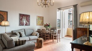 A living room with a sofa, a dining table, and chairs. There is a chandelier, a lamp, and artwork on the walls.