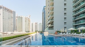 A swimming pool with lounge chairs and umbrellas, surrounded by high-rise buildings. - Relaxing 2BR at Vera Residences (Dubai)