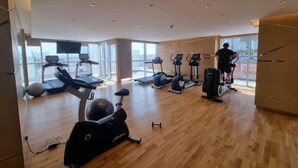 A modern gym with various exercise equipment, large windows, and a high ceiling. - Elegant Studio at Damac Hills Carson B (Dubai)