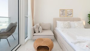A modern bedroom with a sofa, a bed, and a wicker chair. - Elegant Studio at Damac Hills Carson B (Dubai)