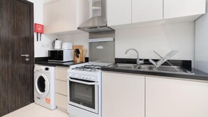 A modern kitchen with white cabinets, a stainless steel range hood, a built-in oven, a microwave, and a double sink. - Elegant Studio at Damac Hills Carson B (Dubai)