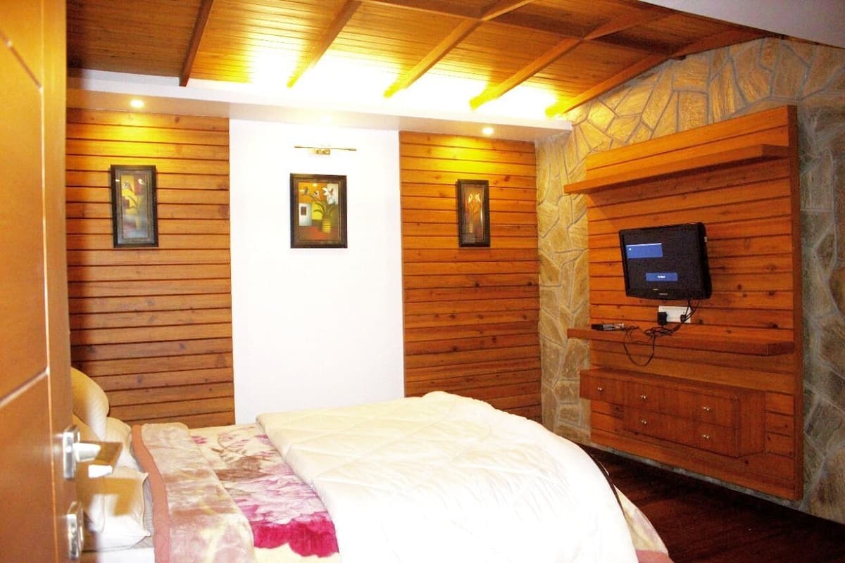 A bedroom with wooden panel walls, a bed with a white and pink blanket, a mounted television, and a stone accent wall.