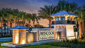 A resort entrance with a sign reading "Windsor Island Resort," featuring a modern building with a blue roof and a small tower-like structure. - Villa near Disney 5 bd/4.5bth home 335 (Davenport)