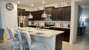 A modern kitchen with dark wood cabinets, stainless steel appliances, and a central island with bar stools. - Villa near Disney 5 bd/4.5bth home 335 (Davenport)