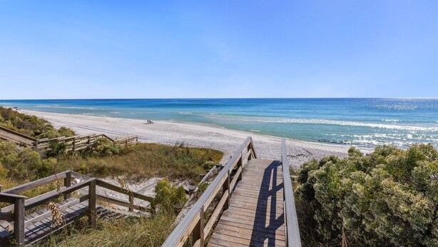 A wooden boardwalk leading to a beach with clear blue water and a sandy shore.