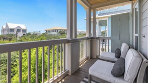 A covered porch with a white bench and cushions, overlooking a residential area with houses and greenery.