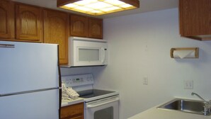 Una cocina compacta con armarios de madera, un refrigerador blanco, un microondas, un horno y un lavamanos.